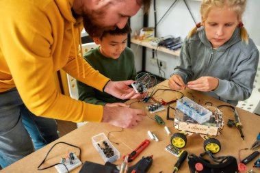 Olmasını sağlamak. Genç teknisyenlerin robot yaparken çekilmiş görüntüsü. Kök robotik dersinde erkek bir öğretmenle birlikte elektrik kablosu setinde çalışıyorlar. Çocuklar için icatlar ve yaratıcılık
