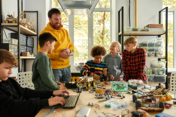Menschen, die Technologie funktionieren lassen. Junge Techniker bauen gemeinsam mit einem männlichen Lehrer in einer Roboterklasse ein Roboterfahrzeug. Erfindungen und Kreativität für Kinder — Stockfoto
