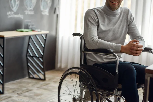 Gehakte foto van lachende mannelijke kantoormedewerker in een rolstoel zittend op zijn werkplek in modern kantoor — Stockfoto