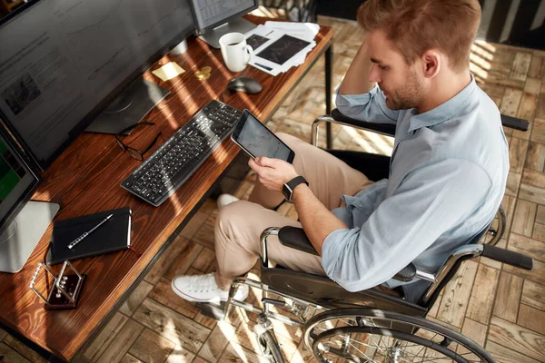 Tekerlekli sandalyede çalışan genç bir ofis çalışanı, ofisinde çalışırken dijital tabletle ilgili verileri analiz ediyor. — Stok fotoğraf