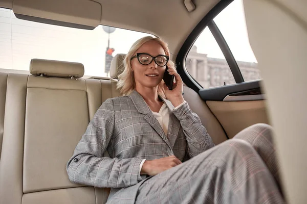 Pozostaję w kontakcie. Piękna bizneswoman w stylowym klasycznym stroju siedzi w samochodzie i rozmawia przez telefon z klientem — Zdjęcie stockowe