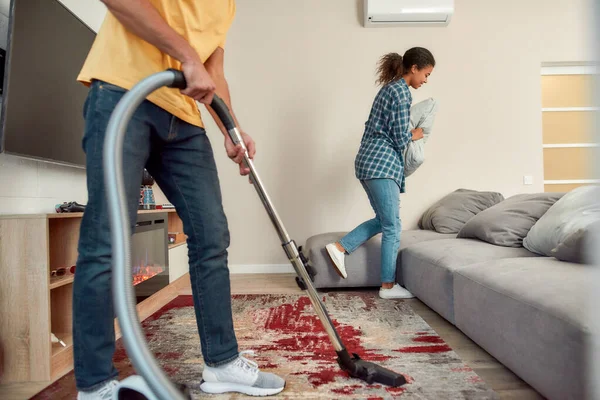 Halten Sie Ihre Familie gesund. Glückliches multikulturelles Paar in lässiger Kleidung, das gemeinsam sein modernes Wohnzimmer putzt. Junger Mann putzt Teppich mit Staubsauger — Stockfoto