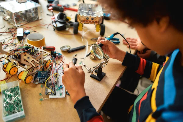 Mejora. Primer plano del joven ingeniero que utiliza el soldador para unir chips y cables. Robótica e ingeniería de software para estudiantes de primaria. Invenciones y creatividad para niños —  Fotos de Stock