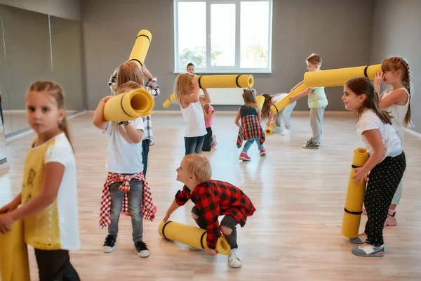 Lezione di ginnastica. Gruppo di bambini carini in abiti casual con tappeti da yoga gialli e divertirsi in piedi nello studio di danza — Foto Stock