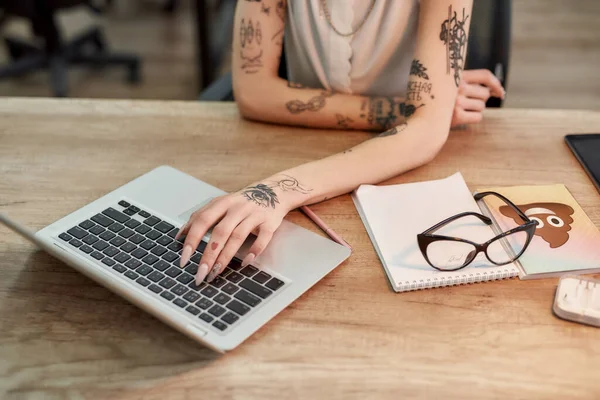 Foto ritagliata di una donna tatuata che digita qualcosa sul portatile mentre lavora in ufficio — Foto Stock