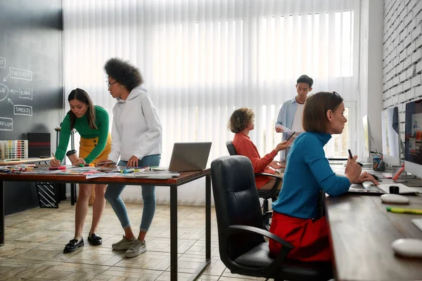 Estudio de diseño. Grupo de jóvenes creativos que trabajan y discuten ideas frescas en la oficina moderna. Diseñadores web en ropa casual trabajando juntos —  Fotos de Stock