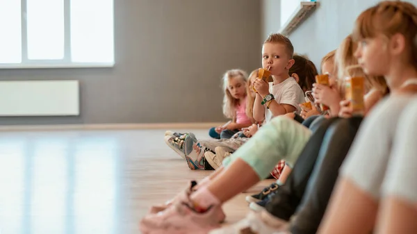 Rilassarsi dopo la lezione di ballo. Gruppo di bambini carini e positivi seduti sul pavimento nella sala da ballo e bere succo di frutta. Mi prendo una pausa. Scuola di danza — Foto Stock