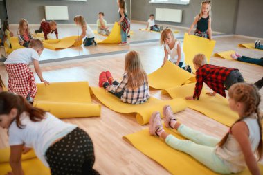 Esnek olmaya başladı. Bir grup çocuk dans stüdyosunda yoga dersine hazırlanıyor.