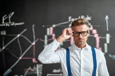 Bugün akıllıca bir hareket yap. Orta yaşlı çalışanlara yakın çekim, kameraya bakan tüccar ve yeni çalışma stratejisini düşünürken çizelgelerle dolu karatahtanın yanında duran. Yatay çekim