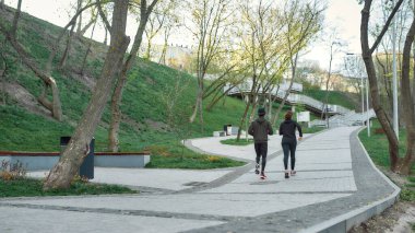 Dışarıda koşuyor. Parkta birlikte koşan siyah spor giysili bir çiftin arka görüntüsü. Sabah kardiyosu