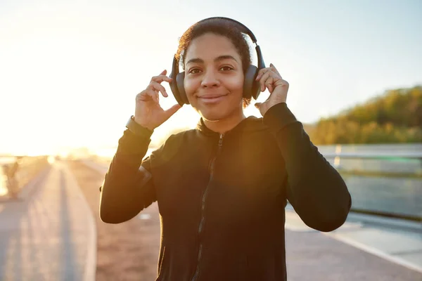 Happy female runner. Positive african female runner wearing headphones, looking at camera and smiling