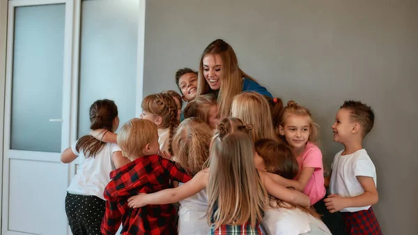 Ung och glad kvinnlig danslärare kramar barn och ler stående i ateljén. Förhållandet mellan lärare och barn. Koreografi klass — Stockfoto