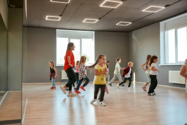 Μαθαίνω χορευτικές φιγούρες με δάσκαλο. Ομάδα μικρών αγοριών και κοριτσιών που χορεύουν ενώ κάνουν μαθήματα χορογραφίας στην σχολή χορού. Γυναίκα δασκάλα χορού και παιδιά — Φωτογραφία Αρχείου