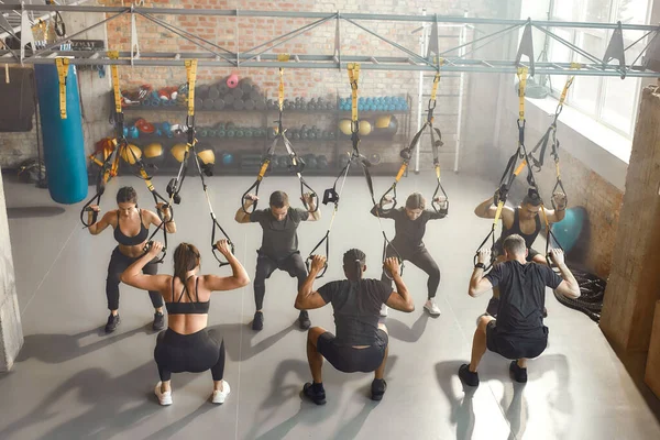 Przestrzeń treningowa. Grupa sportowców wykonująca ćwiczenia fitness TRX na siłowni przemysłowej. Pompa, koncepcja treningu grupowego — Zdjęcie stockowe