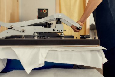 Tüm yazıcı çözümleri için. Erkek işçinin t-shirt yazdırmak için ısı transfer makinesini kullanırken çekilmiş görüntüleri.