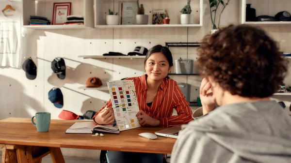 Faire passer les gens avant tout. Portrait de jeune travailleuse montrant des échantillons de couleur de tissu au client masculin dans le bureau. Femme travaillant chez T-shirt personnalisé, entreprise d'impression de vêtements — Photo