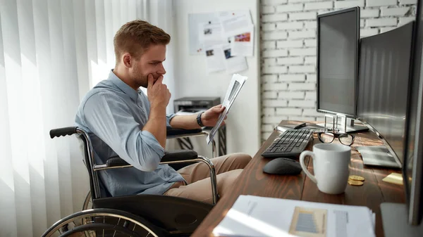 Volledige concentratie. Zijaanzicht van jonge serieuze mannelijke handelaar of zakenman in een rolstoel die het rapport van de aandelengrafiek analyseert terwijl hij op zijn werkplek in het moderne kantoor werkt — Stockfoto