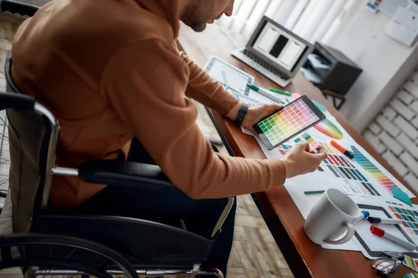 Foto recortada do designer masculino UX UI em uma cadeira de rodas escolhendo as cores certas para o aplicativo móvel enquanto trabalhava em seu local de trabalho criativo no escritório — Fotografia de Stock