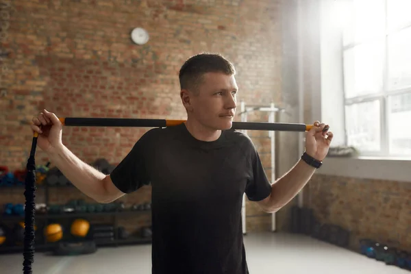 Portare l'attenzione sul fitness. Uomo sportivo guardando da parte, utilizzando pilates esercizio fisico bastone corpo o bar pur avendo allenamento in palestra industriale — Foto Stock