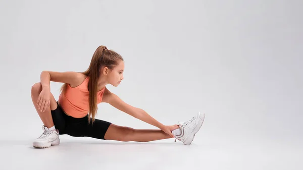 Get Into Healthy Habits. Flexible cute girl child looking at camera while stretching her body isolated on a white background. Sport, training, fitness, active lifestyle concept. Horizontal shot — Stock Photo, Image