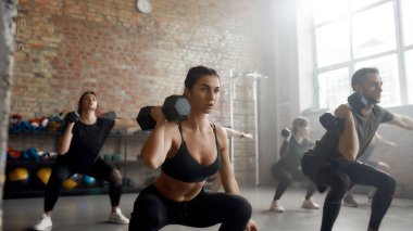 Güçlü oyna. Endüstriyel spor salonunda spor yaparken dambılı kaldıran genç bir kadın. Grup eğitim kavramı
