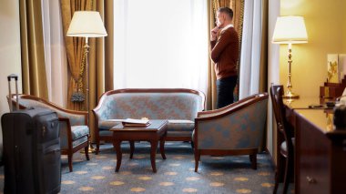 Yüksek seviye deneyim. Girişten sonra otel odasının penceresinin yanında duran iş adamının tam boy görüntüsü. İş gezisi konsepti.