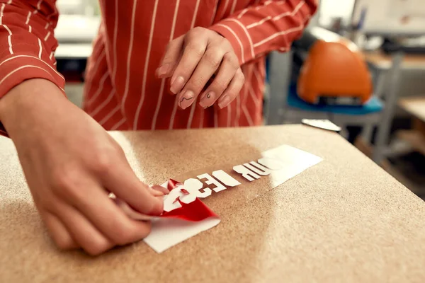 Ord som fungerar. Beskuren bild av kvinna ta bort uppbackning från annons klistermärke med text samtidigt förbereda den för att skrivas ut på en T-shirt — Stockfoto