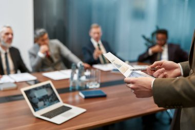 Finansal rapor tutan bir iş adamının bulanık fotoğrafı ve toplantıdayken çok kültürlü iş adamlarına bir şeyler açıklamak.