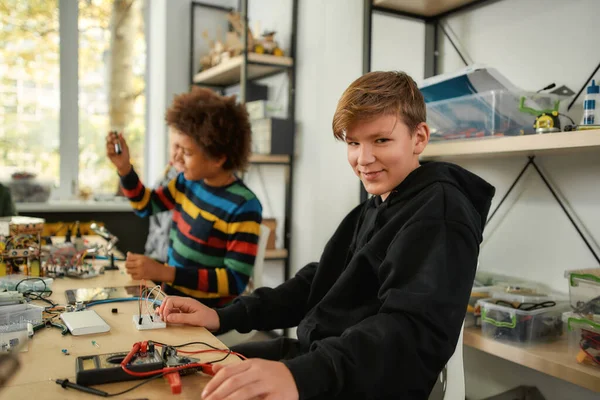 La educación es poder. Niño caucásico mirando a la cámara mientras hace juguetes en una clase de tecnología. Niños inteligentes y educación STEM . —  Fotos de Stock