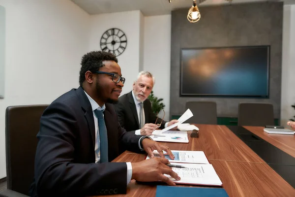 Analizando documentos. Empresarios caucásicos y africanos discuten algo mientras trabajan juntos en la oficina moderna — Foto de Stock