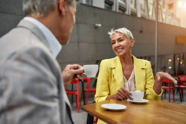 Positive Stimmung. Glückliches und stilvolles älteres Paar, das Kaffee genießt und lächelt, während es auf der Café-Terrasse sitzt. Zeit miteinander verbringen — Stockfoto