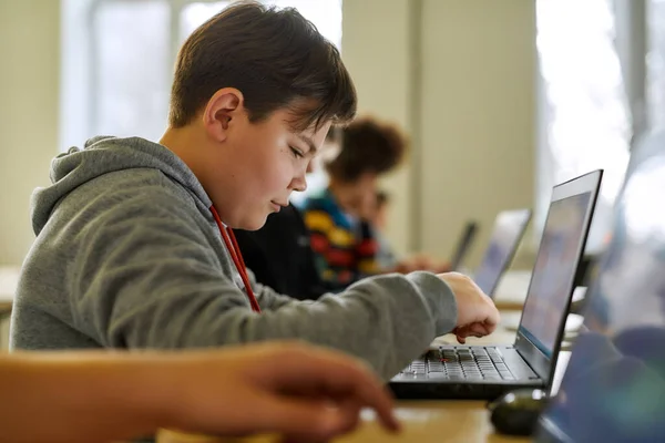 Alunos hoje, líderes amanhã. Close up de estudante caucasiano olhando para a tela do laptop junto com outros alunos durante uma lição na escola inteligente moderna — Fotografia de Stock