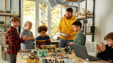 Yüksek performans. Genç yaratıcı erkek öğretmen öğrencilere, konsol kontrolörünü tutarken robotik makinelerin çalışmasının prensibini açıklıyor. Bilim ve eğitim.