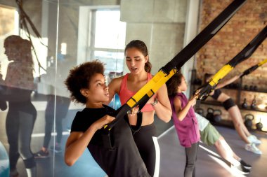 Devam et. Beden eğitiminde spor kayışlarını kullanarak genç bir çocuğa yardım eden kadın çalıştırıcının portresi. Spor, sağlıklı yaşam tarzı, beden eğitimi konsepti