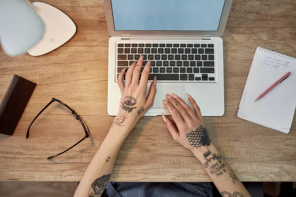 Comodo posto di lavoro. Vista dall'alto delle mani femminili tatuate che lavorano sul laptop. Moderna donna d'affari che digita sulla tastiera mentre lavora in ufficio . — Foto Stock