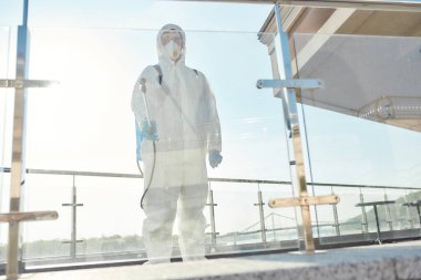 Mikropları temizleyin. Covid19 virüsünün ortaya çıkmasından dolayı şehrin sterilizasyonu, temizliği, dezenfeksiyonu. Koruyucu giysili ve maskeli bir adam iş yerinde, cam yüzeyini temizliyor.
