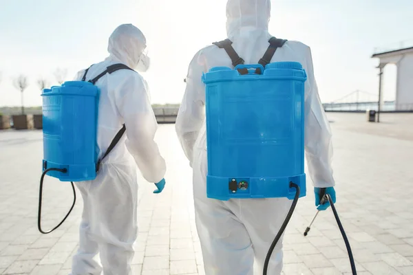 Fast and Reliable. Sanitization and disinfection of the city due to the emergence of the Covid19 virus. Specialized team in protective suits and masks with backpack of pressurized spray disinfectant — Stock Photo, Image