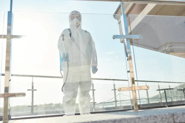 Ta bort bakterier. Sanering, rengöring, desinfektion av staden på grund av uppkomsten av Covid19 viruset. Man i skyddsdräkt och mask på jobbet, sanering glasyta — Stockfoto