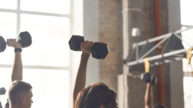 Endüstriyel spor salonunda çalışan bir kadın dambılı kaldırıyor. Grup eğitimi, takım çalışması konsepti