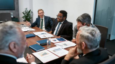 Başarılı bir takım. Çok kültürlü iş adamları modern ofiste toplantı yaparken bir şeyler tartışırlar.