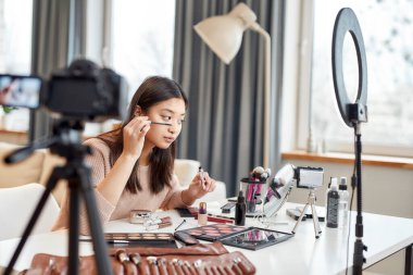 Yaratıcı süreç. Asyalı kadın blogcu makyaj tekniklerini ve sırlarını gösteriyor. Güzellik blogu için evde kamera kullanarak özel bir video kaydediyor.