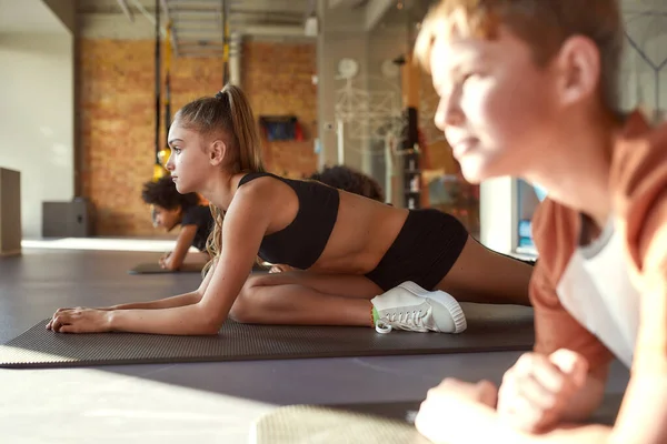 Traz a tua flexibilidade. Retrato de menina tentando pose de ioga, fazendo exercícios em conjunto com outras crianças no ginásio. Alongamento em um dia ensolarado. Esporte, estilo de vida saudável, conceito de educação física — Fotografia de Stock