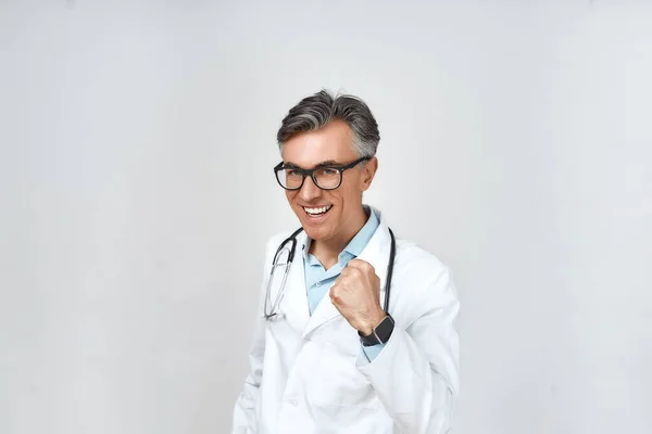 Portré izgatott boldog férfi orvos orvosi egyenruhában mosolyog és ünnepli a siker, mutatnak igen gesztus, miközben áll szemben szürke háttér — Stock Fotó