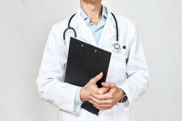 Γιατρός στη δουλειά. Καλλιεργημένη φωτογραφία του επαγγελματία γιατρού με ιατρική στολή με στηθοσκόπιο γύρω από το λαιμό κρατώντας μαύρο χάρτινο φάκελο, στέκεται πάνω σε γκρι φόντο — Φωτογραφία Αρχείου