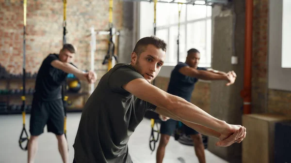 Hazte más fuerte que tus excusas. Retrato de diversos hombres atléticos que estiran el cuerpo mientras hacen ejercicio juntos en el gimnasio industrial. Concepto de formación en grupo — Foto de Stock