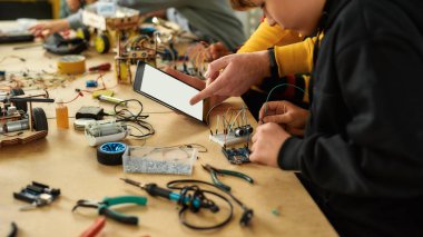 Büyük düşün. Kök robotik dersinde kablo takımıyla çalışan genç teknisyenlerin görüntüsü. Erkek öğretmen onlara yardım ediyor, tavsiye veriyor, tablet bilgisayar kullanıyor. Çocuklar için icatlar ve yaratıcılık