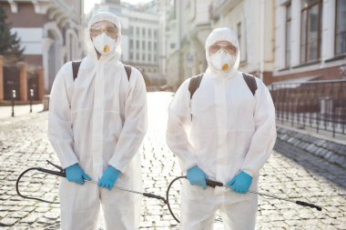 Emergency crew. Sanitization, cleaning and disinfection of the streets and alleys in the city center due to the emergence of the Covid19 virus. Men in protective suits and masks at work clipart