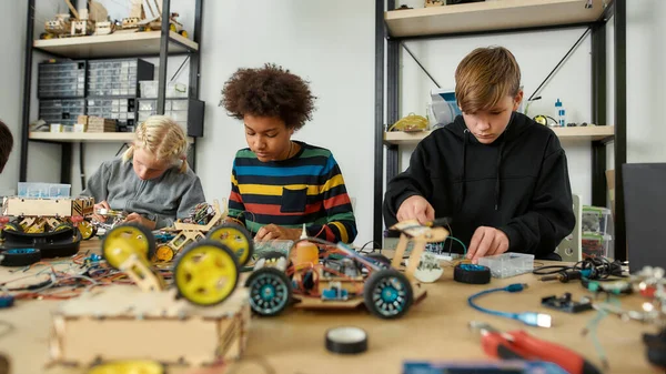 Tapasztalat. Precíz. Kiválóság. Három gyerek robotokat és járműveket épít robotika órán. Okos gyerekek és STEM oktatás. — Stock Fotó