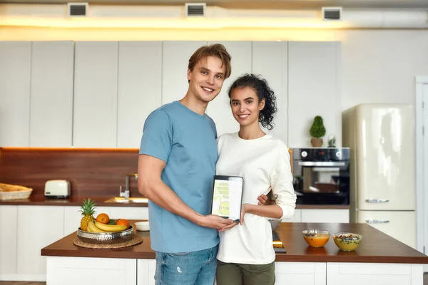 Για υγιές σώμα. Ευτυχισμένο ζευγάρι, χορτοφάγοι χαμογελούν στην κάμερα ενώ στέκονται στην κουζίνα μαζί. Νεαρός άνδρας και γυναίκα κρατώντας tablet pc. Χορτοφαγία, υγιεινά τρόφιμα, διατροφή, τεχνολογική έννοια — Φωτογραφία Αρχείου