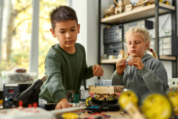 Imaginem, Inventar, Inspirar. Menino asiático e menina caucasiana fazendo seus próprios veículos em uma classe de robótica de tronco. Invenções e criatividade para crianças . — Fotografia de Stock